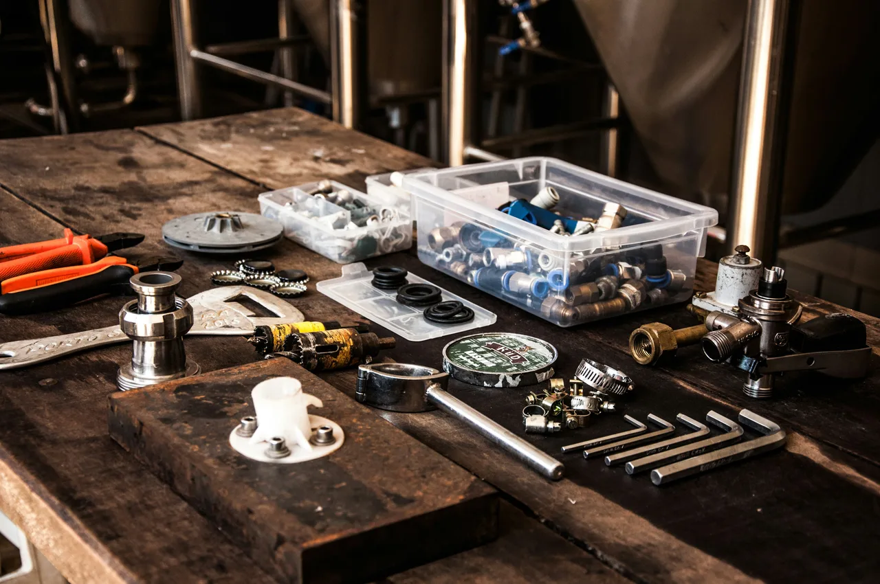 Plumbing fittings, pliers, hex keys and small parts arranged on a worn wooden workbench.
