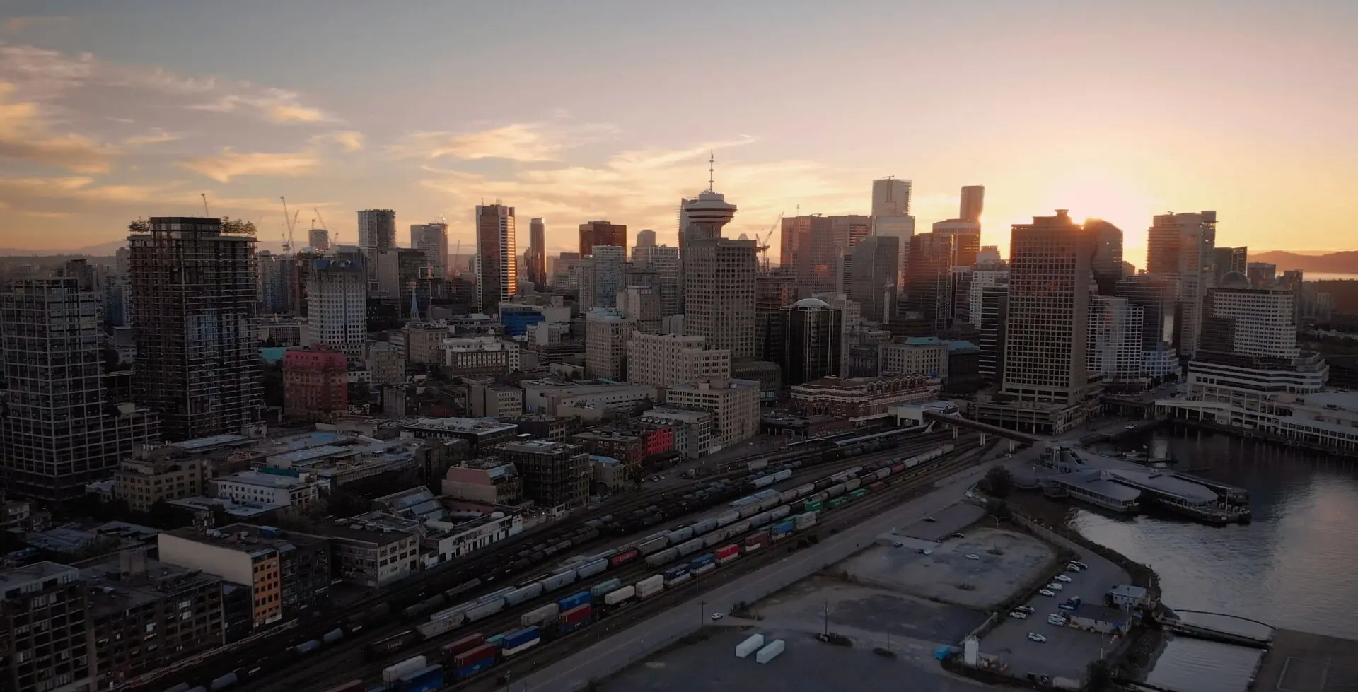 Vancouver skyline at sunset above waterfront rail tracks and rows of freight cars.