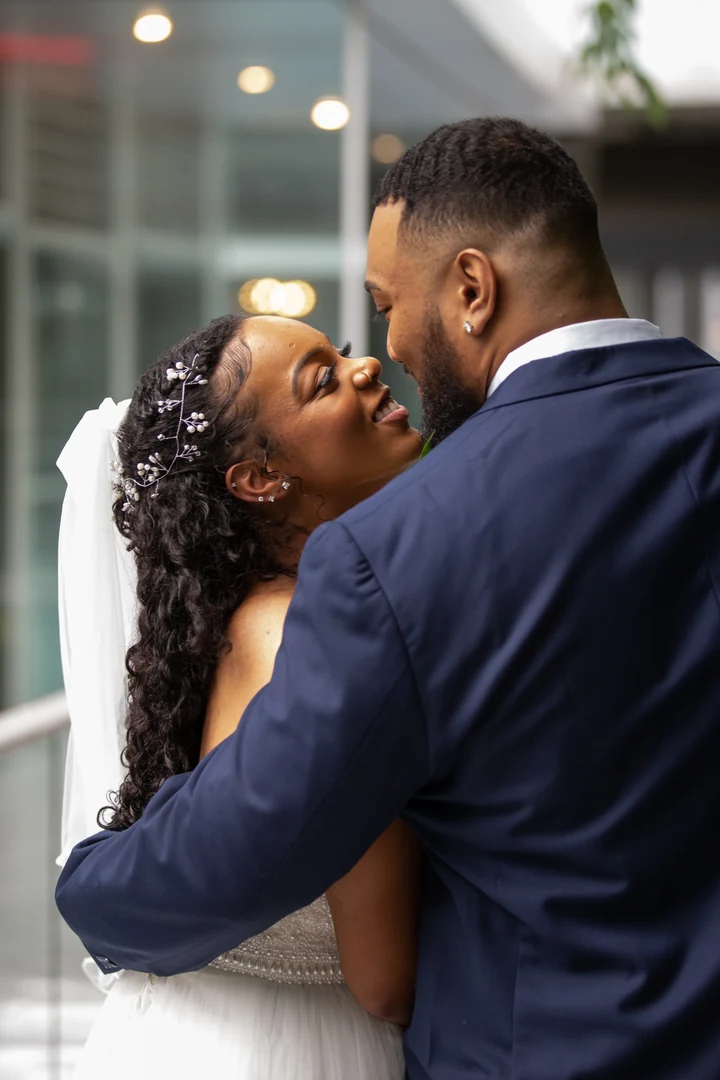 Close wedding portrait of the couple embracing beside a glass building, with the bride looking up toward the groom.
